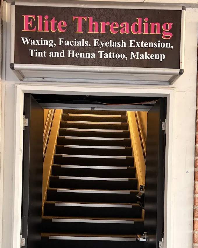 The pink and charcoal Elite Threading sign above the open entrance and lit stairs