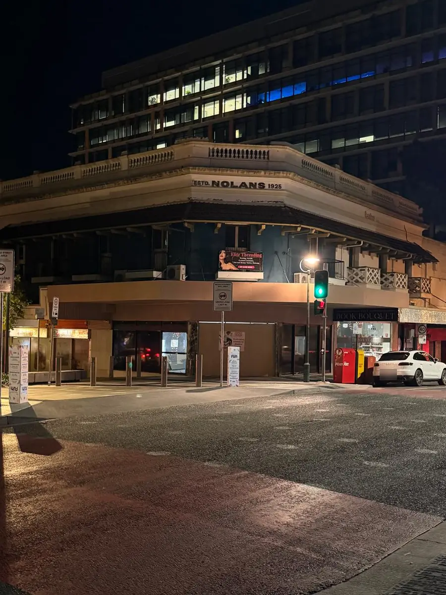 The corner building on Nicholas St at night, with the Elite Threading sign lit on the first floor