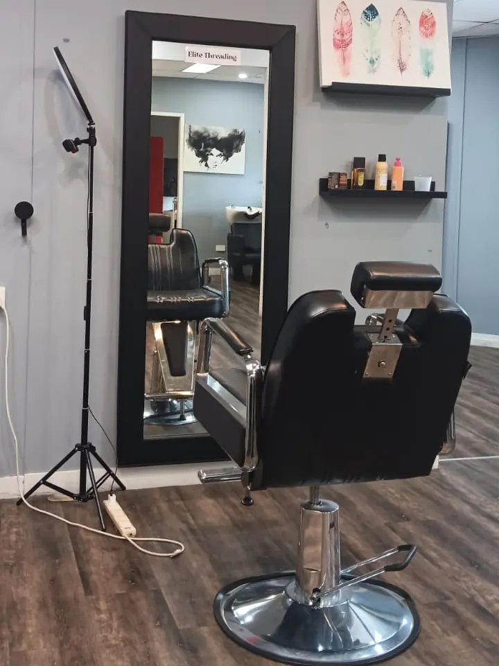Our brow chair, a black reclining salon chair facing a tall mirror that holds an Elite Threading card